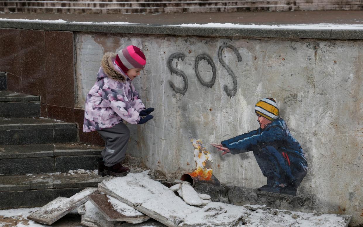 Anastasia, 4, stands next to an artwork of the famous street artist Tvboy in the town centre outside Kyiv - VALENTYN OGIRENKO/REUTERS