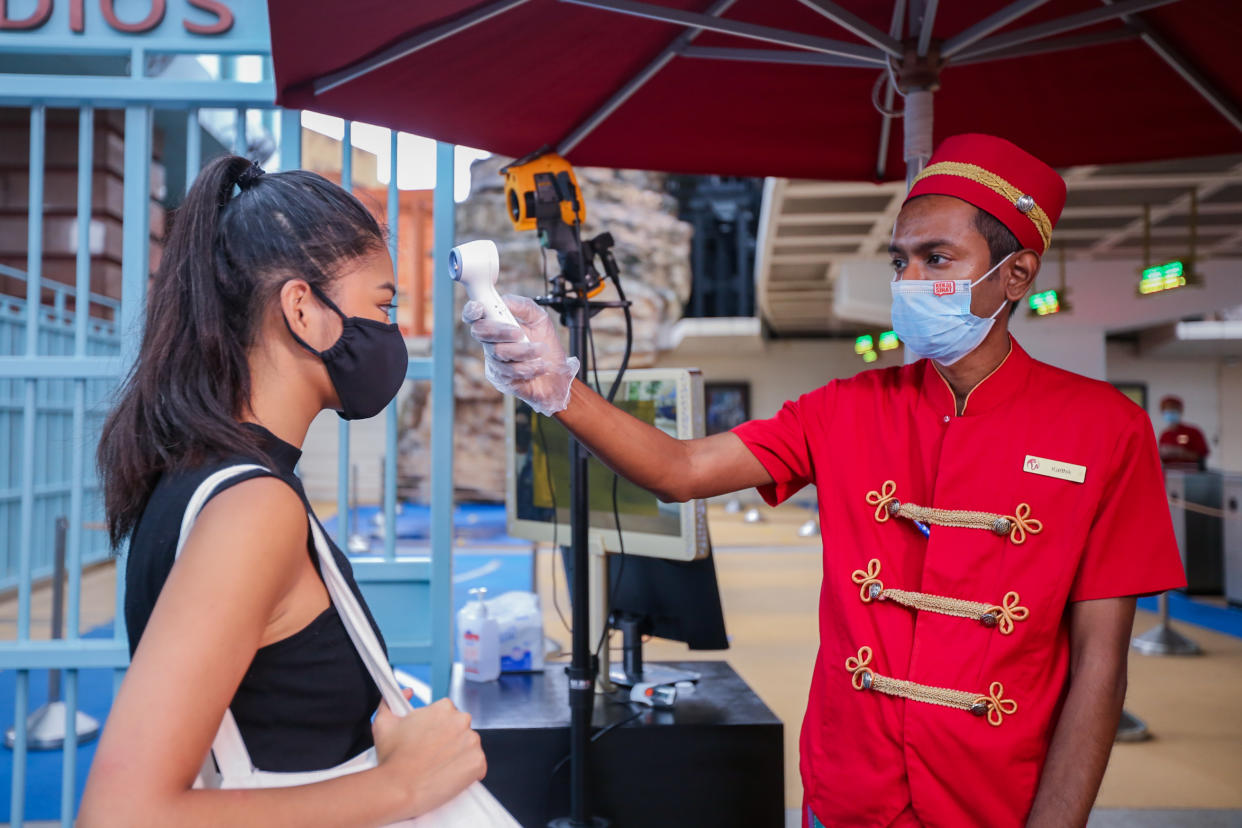 A posed photo of a Universal Studios Singapore employee checking the temperature of a guest with a thermometer. Resorts World Singapore attractions on Sentosa, including Universal Studios Singapore and the S.E.A. Aquarium, will reopen in Phase 2 of Singapore's reopening during the COVID-19 pandemic. (Photo: RWS)