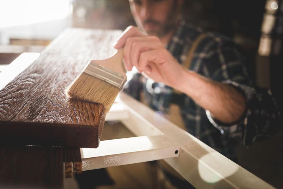 A man uses a brush to refinish a piece of furniture. 