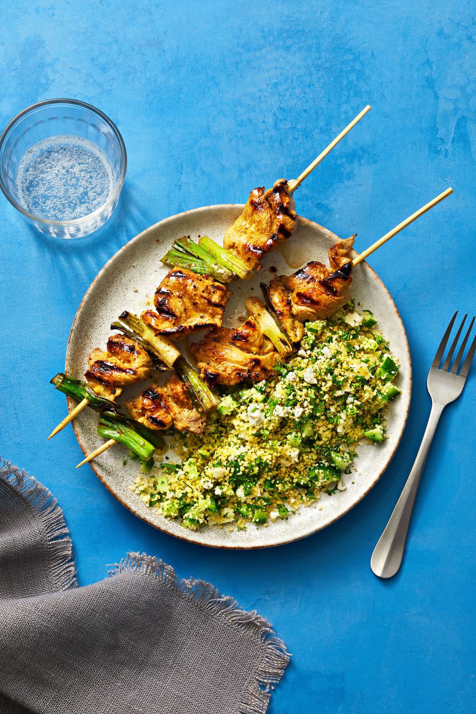 pork skewers on a plate with herby couscous