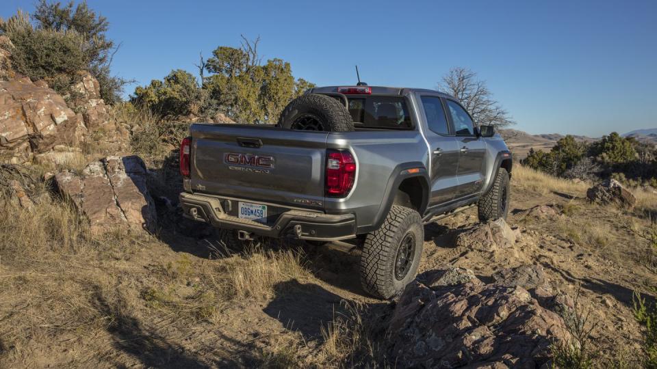 rear 34 view of the 2024 gmc canyon at4x aev edition climbing a rock, showcasing the additional aev in bed vertical spare tire mount