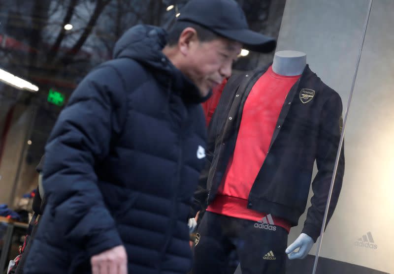 Man walks past an Adidas shop window where a model is dressed in sports outfit with English soccer club Arsenal's logo in Beijing
