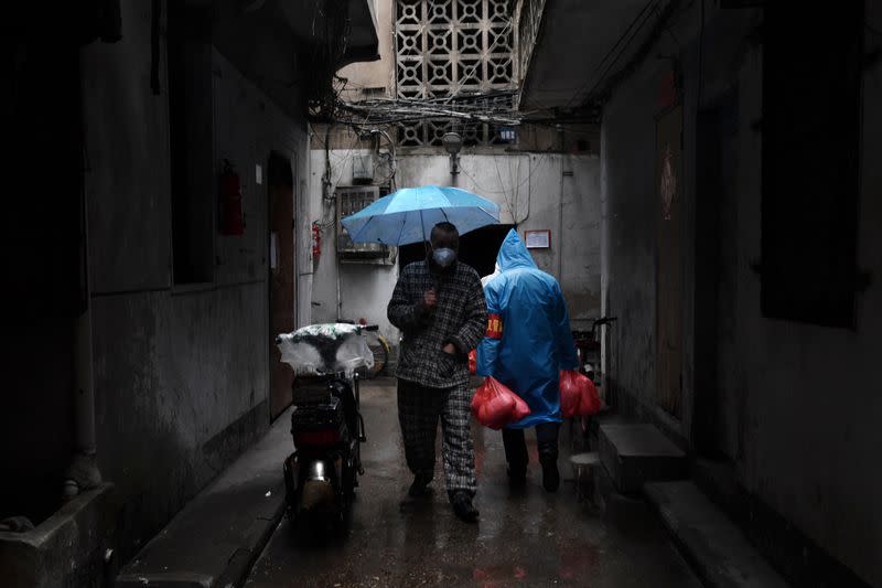 Man wearing a face mask walks past a volunteer carrying food at a residential area in Wuhan