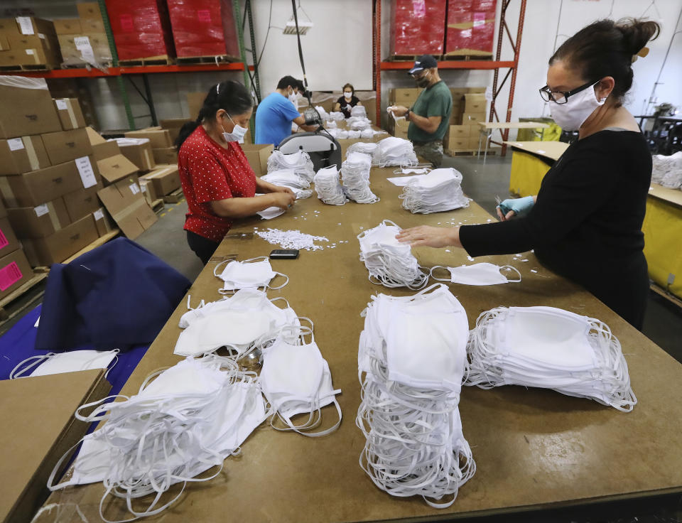 In this Thursday, April 23, 2020 photo, Kenia Anzarado, right, and Mae Catalan, left, works on finishing and packing face masks at the Georgia Expo in Suwanee, Ga. The company has pivoted from sewing curtains to sewing cloth face masks. As business restrictions ease companies are preparing to open, but one key ingredient to safety is nearly impossible to find, personal protective equipment. (Curtis Compton/Atlanta Journal-Constitution via AP)