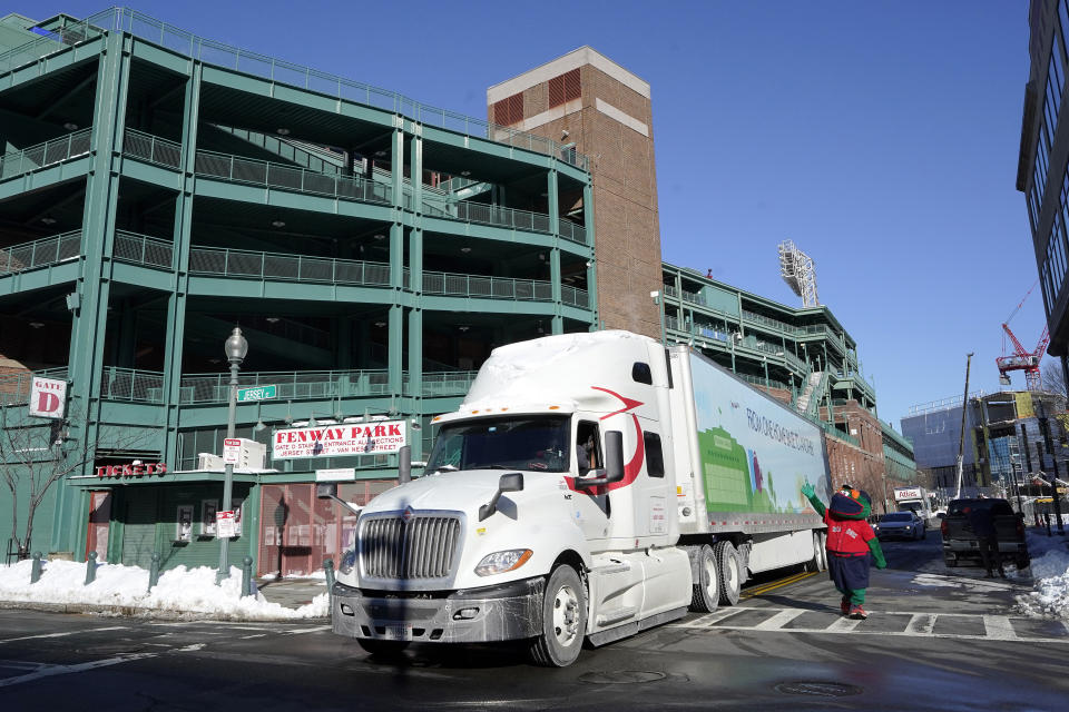 Wally the Green Monster, the team's mascot, right, waves as a Boston Red Sox baseball equipment truck departs Fenway Park, Monday, Feb. 8, 2021, in Boston on its way to the team's spring training facility, in Fort Myers, Fla. (AP Photo/Steven Senne)