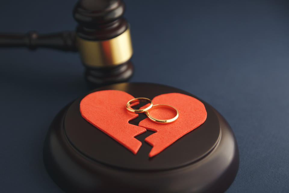 A judge's gavel sits next to two wedding rings placed on a broken heart symbol, representing divorce or separation