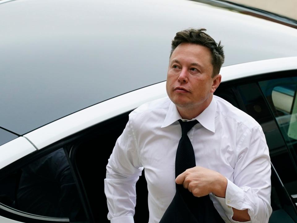 Tesla CEO Elon Musk in a white shirt and tie exits the backseat of a white Tesla