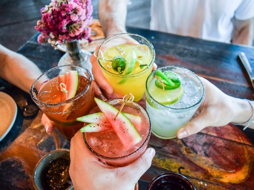 Friends toasting, saying cheers holding tropical blended fruit margaritas. Watermelon and passionfruit drinks. - Image