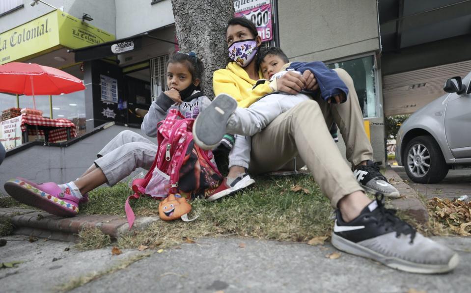 Woman sits with her two children at the base of a tree