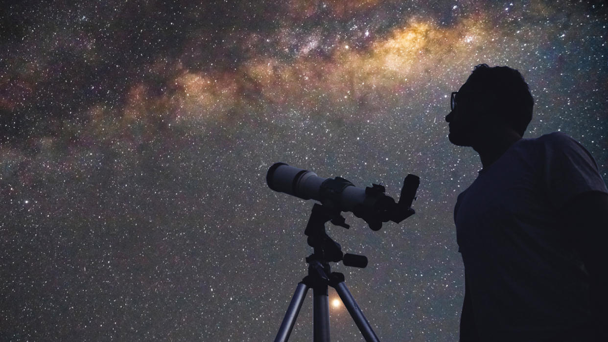 Silhouette of an astronomer with a telescope gazing at the night sky.