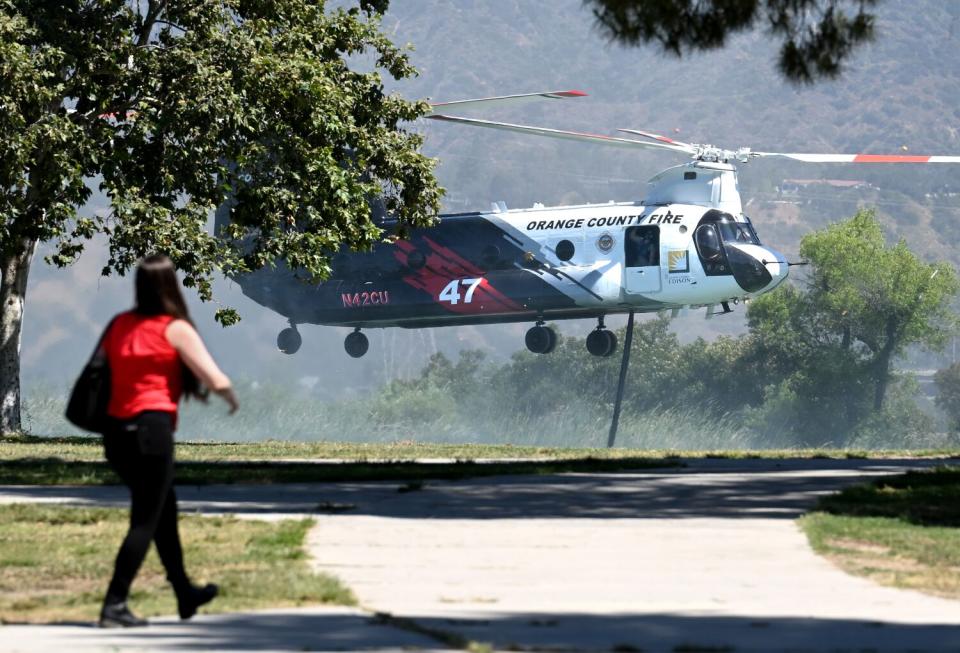 A person walks in the foreground as a black and white helicopter hovers close to ground in the background.