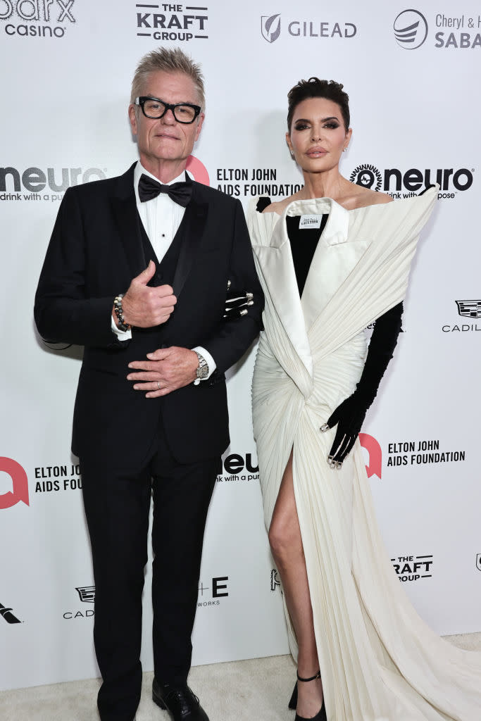 Harry Hamlin, in a tuxedo, and Lisa Rinna, in an elegant off-shoulder gown with a thigh-high slit, pose together at the Elton John AIDS Foundation event