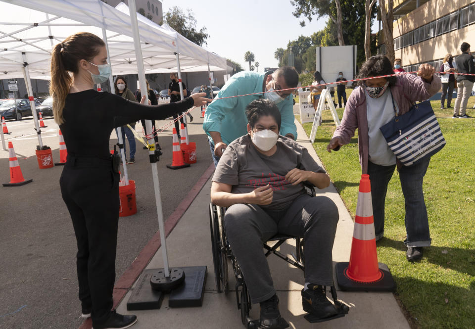 St. John's Well Child and Family Center facilities coordinator Raul Chiriboga, middle, helps Joel Flores, 36, who suffers from autism, and his mother, Emilia del Carmen Flores, 75, originally from El Salvador, get through with the wheelchair at the COVID-19 vaccination site at the East Los Angeles Civic Center in Los Angeles, Thursday, March 4, 2021. California will begin setting aside 40% of all vaccine doses for the state's most vulnerable neighborhoods in an effort to inoculate people most at risk from the coronavirus more quickly. (AP Photo/Damian Dovarganes)