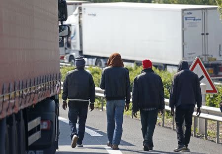 Migrants walk near trucks blocked on a road which leads to the Channel Tunnel terminal in Coquelles near Calais, northern France, July 1, 2015. REUTERS/Vincent Kessler