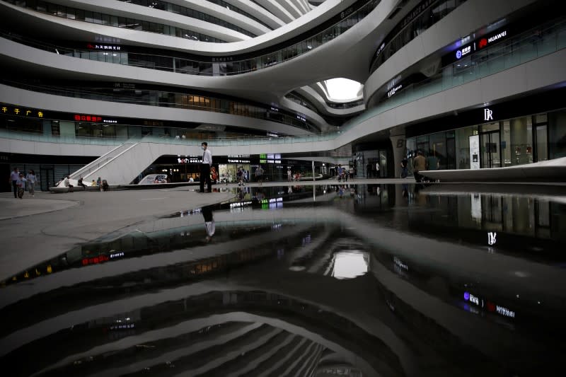 FILE PHOTO: A member of security personnel wearing a face mask stands guard as the Galaxy SOHO office and commercial buildings are reflected in the water in Beijing