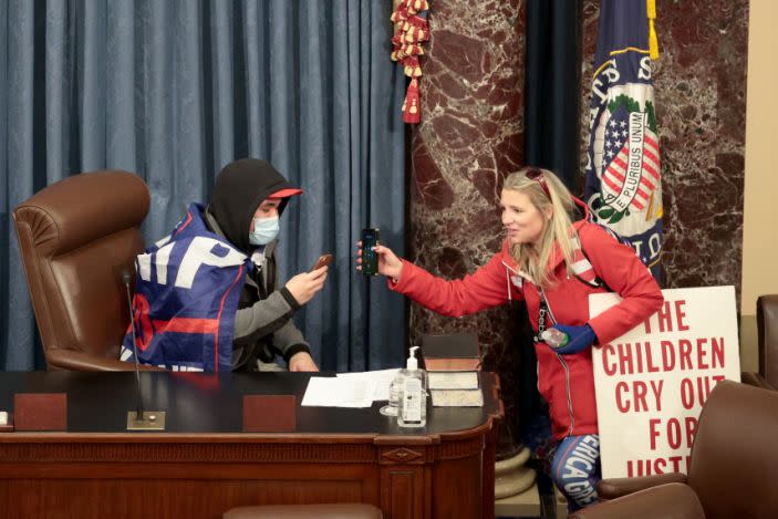 Christine Priola sostiene un teléfono en su mano mientras un manifestante se sienta en la cámara del Senado el 6 de enero de 2021 en Washington D. C. (Win McNamee / Getty Images).