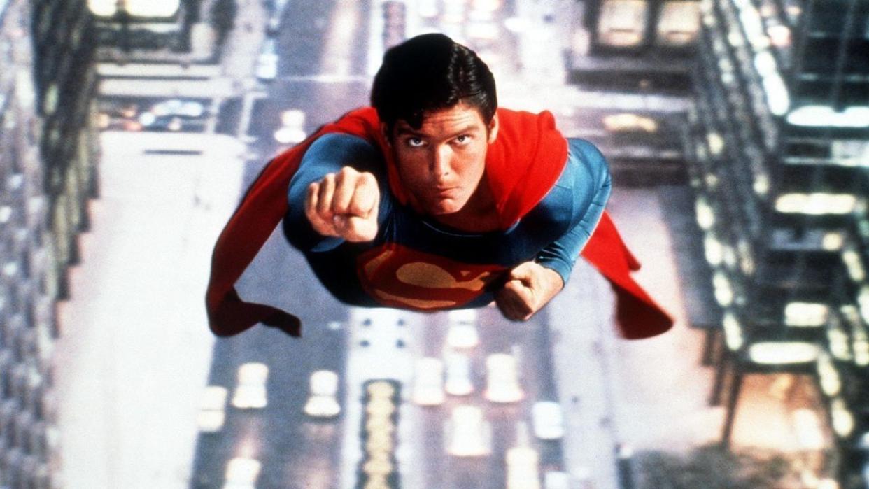 actor christopher reeve as superman flying through the air in his iconic blue and red superhero costume with a red cape