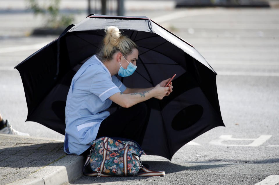 A woman uses an umbrella to shelter from the sun as she waits for a Coronavirus test outside a community centre in Bury, England following the outbreak of the coronavirus disease.