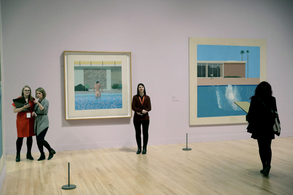 People stand near David Hockney's "Peter Getting out of Nick's Pool", left, and "A Bigger Splash" during a photocall to promote the largest-ever retrospective of his work at Tate Britain gallery in London, Monday, Feb. 6, 2017. The exhibition, which opens to the public from February 9 and runs until May 29, celebrates the 79-year-old's achievement in painting, drawing, photography and video. (AP Photo/Matt Dunham)
