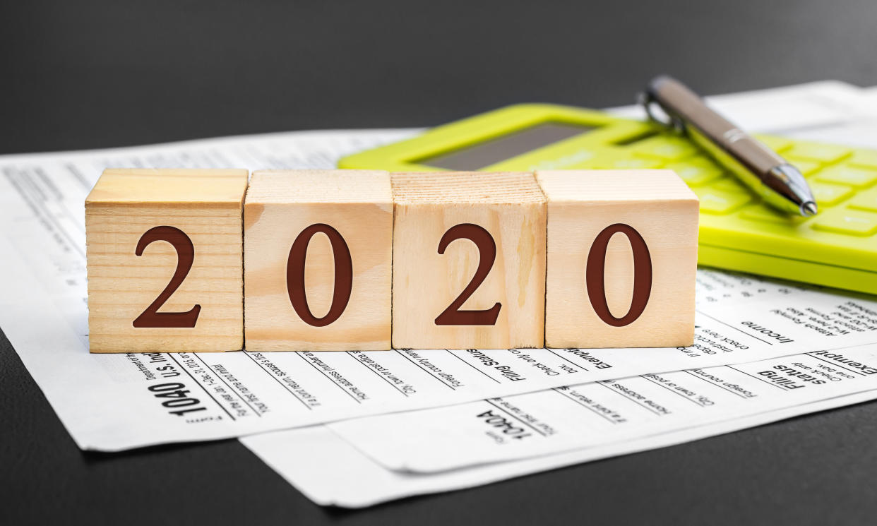 Pay tax in 2020. Wooden cubes with numbers of 2020 year, tax forms and calculator on black.
