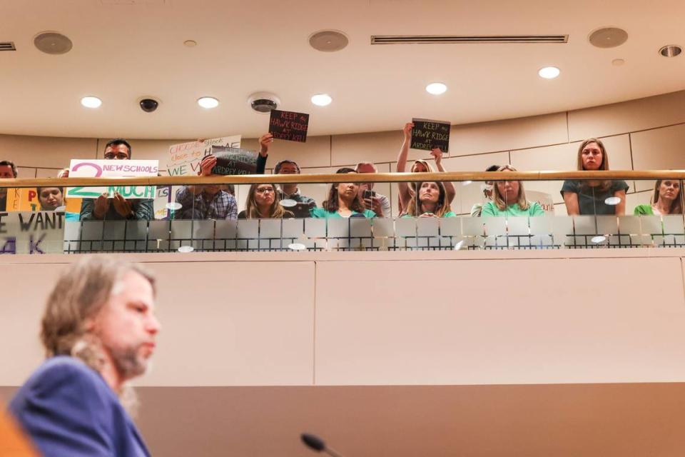 Parents hold signs up as Dennis LaCaria, a CMS official, speaks during a board of education meeting on Tuesday, April 23, 2023 at the Charlotte Mecklenburg Government Center.