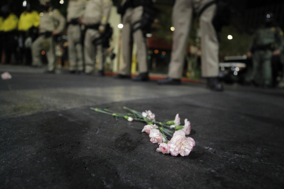Flowers, left by protesters, lie on the ground at the feet of police officers at a rally Monday, June 1, 2020, in Las Vegas, over the death of George Floyd, a black man who died May 25 after being detained by police in Minneapolis. (AP Photo/John Locher)