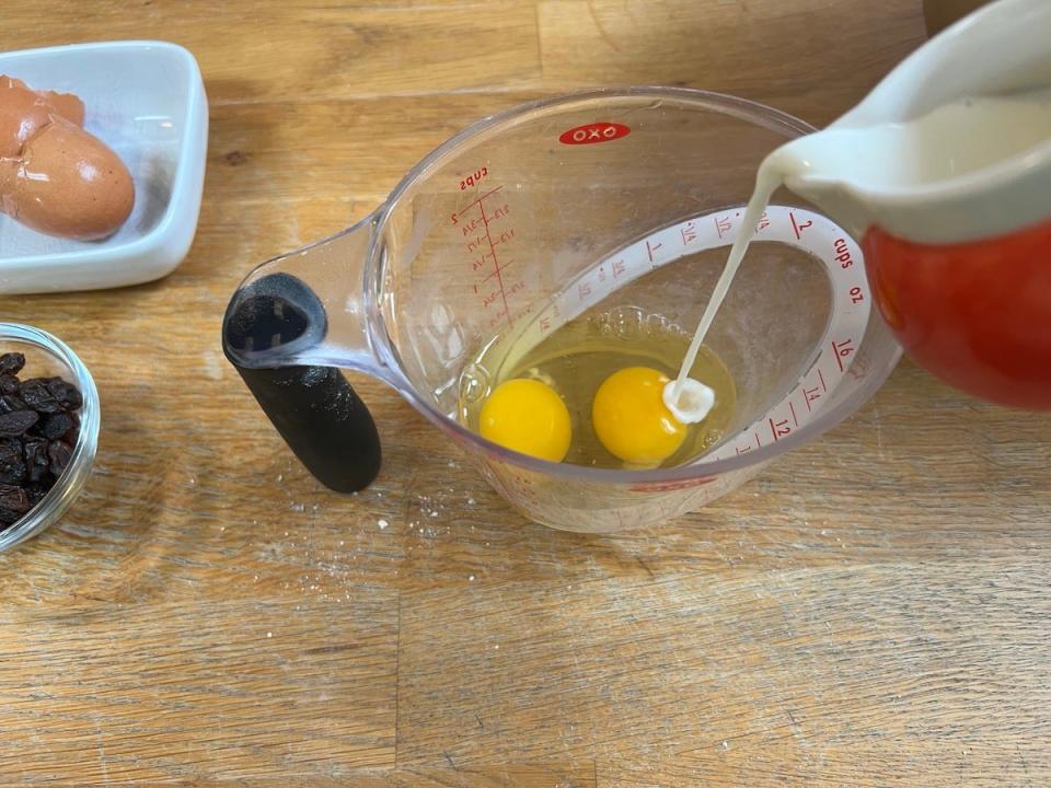 An overhead shot shows milk from a jug being poured into a Pyrex measuring jug that contains two eggs.