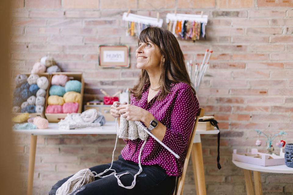 smiling woman sitting on chair knitting