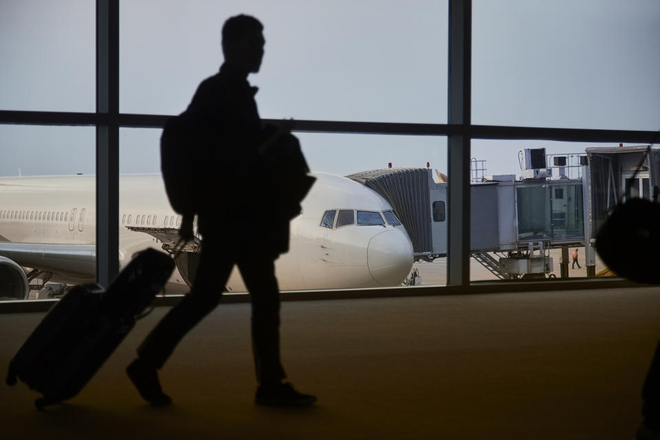 A passenger is in the shadow walking past a commercial aircraft docked to an airport terminal