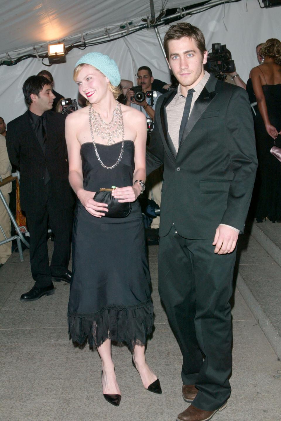 Kirsten Dunst in a black dress and hat and Jake Gyllenhaal in a suit on a red carpet.