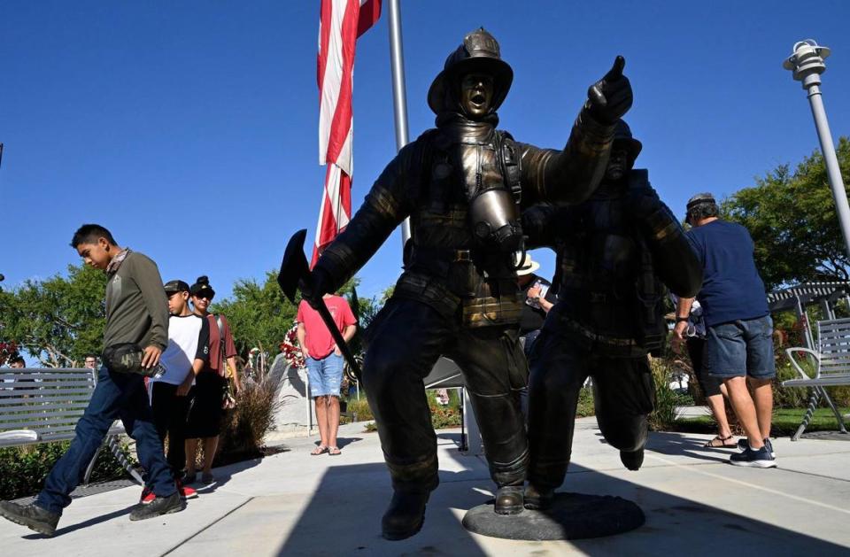 Sunlight cuts through tall stone replicas of the Twin Towers highlighting a bronze sculture of two firemen, seen following the annual Memorial Ceremony at the California 9/11 Memorial Monday morning, Sept. 11, 2023 in Clovis.