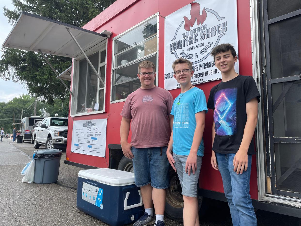Teenage brothers Alexander (center) and Jacob Alexander Kova (right) came up with the idea for their family's new food truck, Two Brothers BBQ Mac Shack, with their father John O'Brien, shown at Pinckney's rally Friday, July 23, 2021.