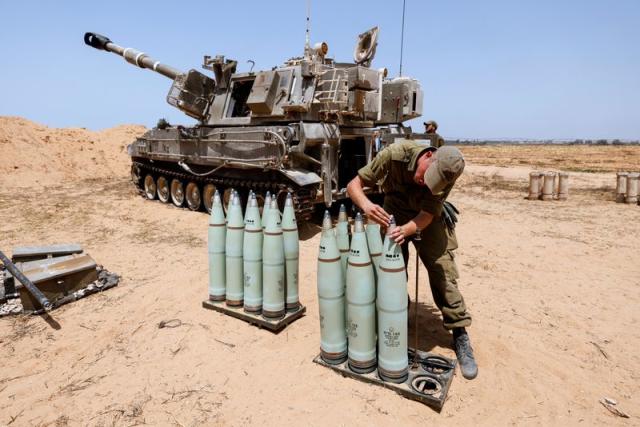 An Israeli soldier checks ammunition next to a mobile artillery unit in a field on the Israeli side of the border with the Gaza Strip