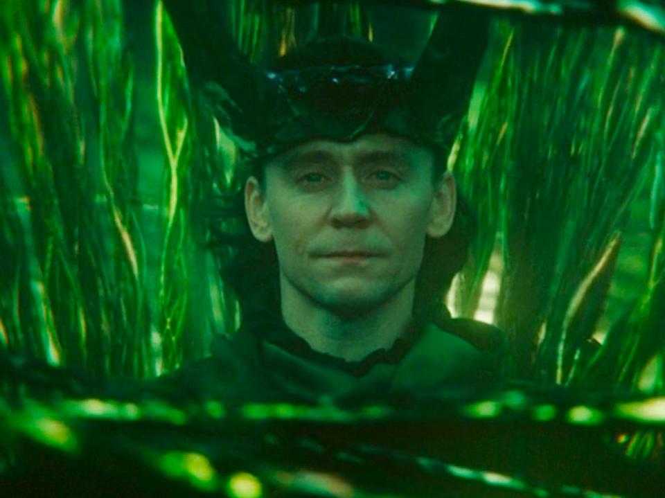 Tom Hiddleston as Loki sitting on a throne surrounded by green timelines.