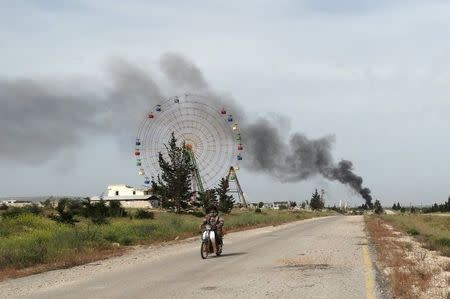 A rebel fighter rides a motorbike along a road in Qarmeed camp, as smoke rises in the background after Islamist rebel fighters took control of the area from forces of Syria's President Bashar al-Assad, April 27, 2015. REUTERS/Abdalghne Karoof