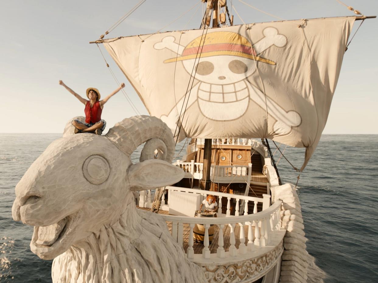 iñaki godoy as luffy in one piece, sitting on his ship's ram figurehead with his arms outstretched