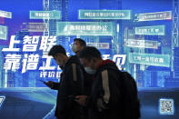 Commuters wearing face masks to help curb the spread of the coronavirus browse their smartphones as they walk by a mobile phone app advertisement at a subway station in Beijing Tuesday, March 2, 2021. Chinese leaders are shifting focus from the coronavirus back to long-term goals of making China a technology leader at this year's highest-profile political event, the meeting of its ceremonial legislature, amid tension with Washington and Europe over trade, Hong Kong and human rights. (AP Photo/Andy Wong)