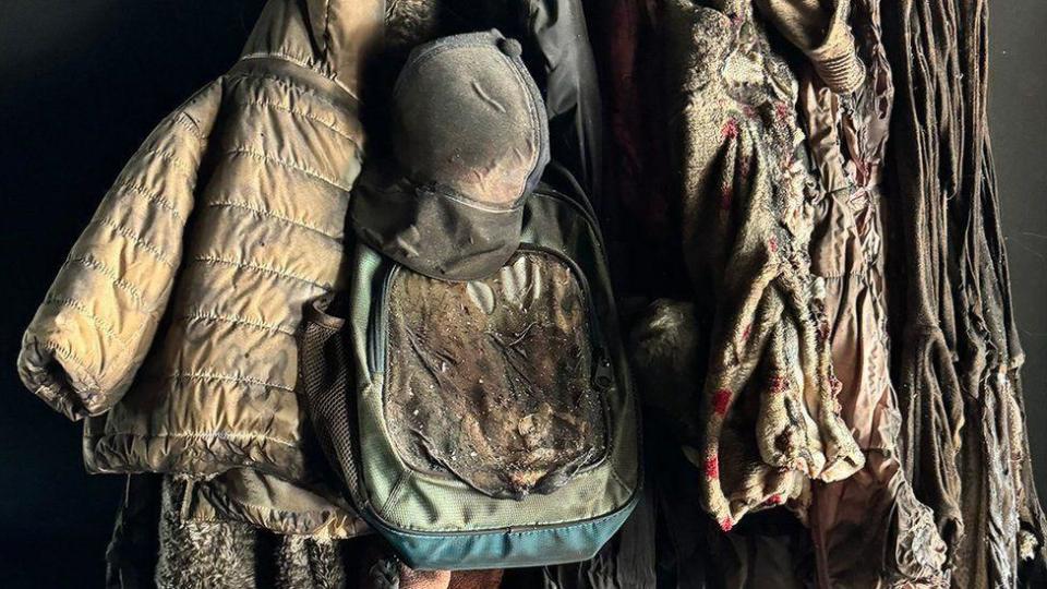 Varias chaquetas de niños y una mochila todavía cuelgan de la pared de una casa que fue incendiada.