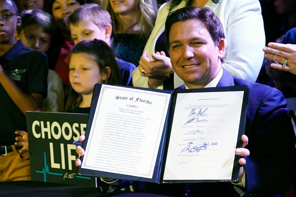 Florida Gov. Ron DeSantis holds up a 15-week abortion ban law after signing it, Thursday, April 14, 2022, in Kissimmee, Fla.  The move comes amid a growing conservative push to restrict abortion ahead of a U.S. Supreme Court decision that could limit access to the procedure nationwide.  (AP Photo/John Raoux)