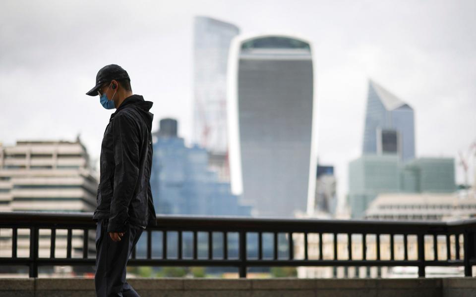 The City of London financial district is seen as a man wearing a protective face mask walks along the River Thames - HENRY NICHOLLS /REUTERS