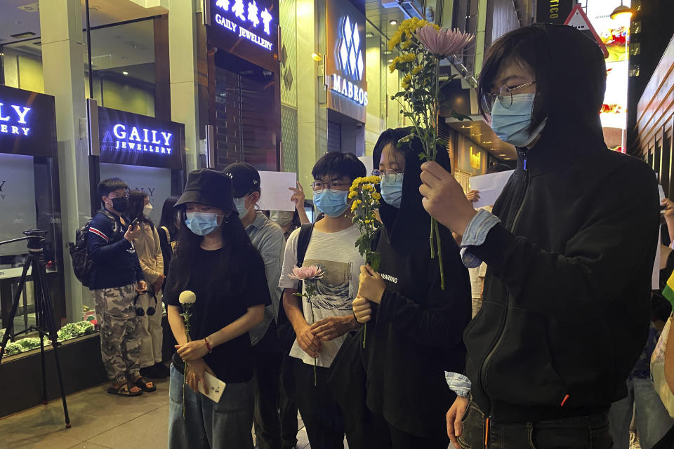Residents hold up flowers to commemorate victims of a recent Urumqi deadly fire in Central in Hong Kong, Monday, Nov. 28, 2022. Students in Hong Kong chanted “oppose dictatorship” in a protest against China’s anti-virus controls after crowds in mainland cities called for President Xi Jinping to resign in the biggest show of opposition to the ruling Communist Party in decades. (AP Photo/Zen Soo)