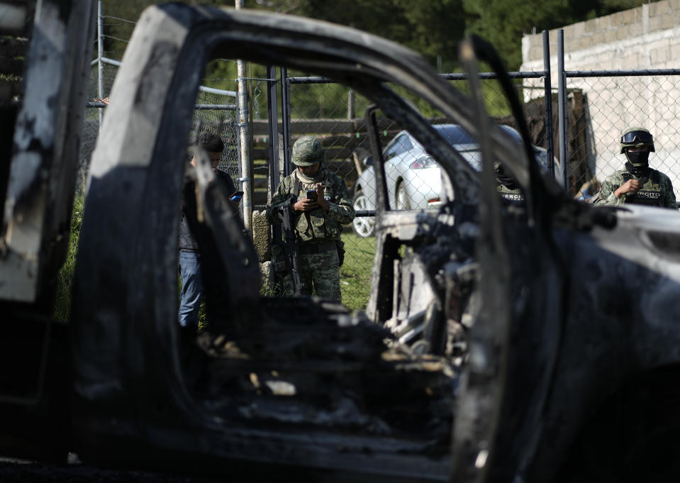 A Mexican Army soldier checks his phone as he stands near the burnt-out remains of a truck that was torched during a protest against a raid targeting illegal logging and sawmills in the pine forests outside of Huitzilac, Mexico, Wednesday, Aug. 2, 2023. Morelos state prosecutors said the raid involved at least 300 officers of the state police, the National Guard and the army. (AP Photo/Eduardo Verdugo)