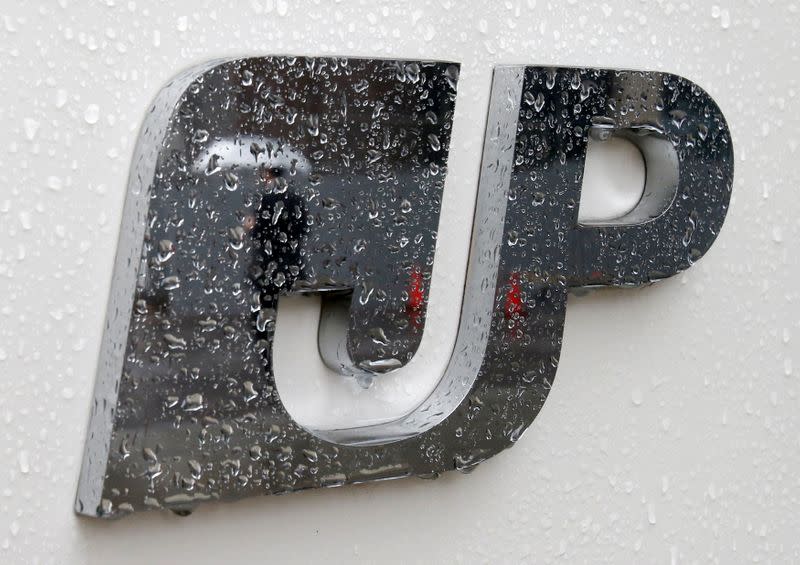 FILE PHOTO: FILE PHOTO:A man holding an umbrella is reflected in the logo of Japan Post Group at its headquarters in Tokyo