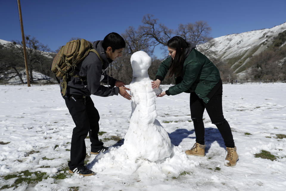 Michael Monsivais, left, makes a snow man with the help of his girlfriend Torrie Martinez at Fort Tejon State Historic Park, Monday, Feb. 11, 2019, in Lebec, Calif. A series of winter storms socked the U.S west with unusual snow also falling in Hawaii and parts of Southern California. (AP Photo/Marcio Jose Sanchez)