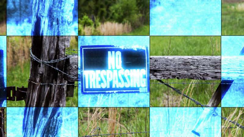 Wood and wire fence on a farm with a No Trespassing sign, as seen through a camera.