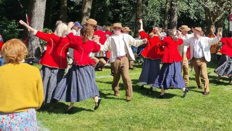 Women in blue Manx kilts and red jackets dancing with men in straw hats and suits