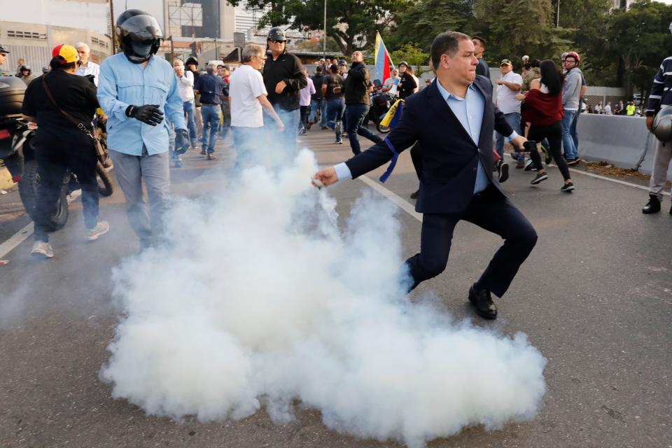 An opponent to Venezuela's President Nicolas Maduro returns a tear gas canister to soldiers who launched it at a small group of civilians and rebel troops gathered outside La Carlota air base in Caracas, Venezuela, Tuesday, April 30, 2019. Venezuelan opposition leader Juan GuaidÃ³ took to the streets with activist Leopoldo Lopez and a small contingent of heavily armed troops early Tuesday in a bold and risky call for the military to rise up and oust socialist leader Nicolas Maduro. (AP Photo/Ariana Cubillos)