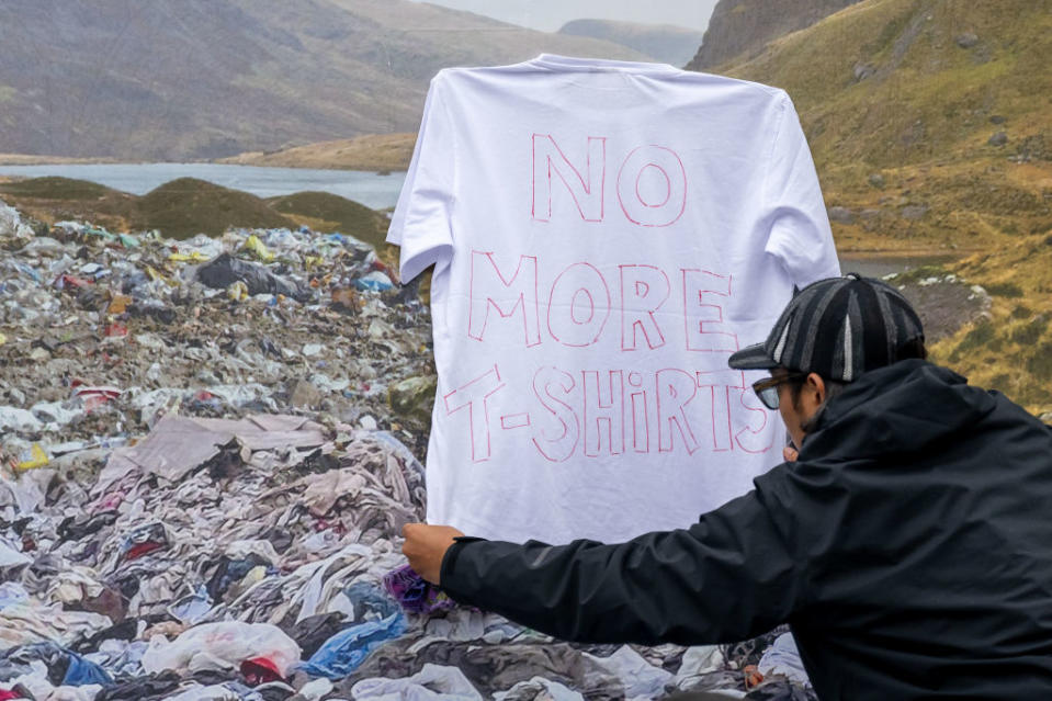 BRISTOL, ENGLAND - AUGUST 25: A man pins a t-shirt with "no more t-shirts" printed onto the front onto a board showing landfill dumped at a beauty spot at the Act 1.5 concert at Clifton Downs on August 25, 2024 in Bristol, England. Long-time climate campaigners Robert Del Naja and Grant Marshall of the band Massive Attack had the idea to stage a low-carbon gig compatible with the Paris 1.5 climate change agreement but the Covid-19 pandemic delayed it. Tonight, Act 1.5 in their home city of Bristol sees the culmination of their work with climate scientists from the Tyndall Centre for Climate Change Research to realise their desire to provide a blueprint for decarbonisation of the Live Music Sector. Partners companies Zenobe, UN Race to Zero, Ecotricity and Train Hugger are providing an entire site powered by 100% renewable energy, a meat-free arena, free pre and post-show shuttles to main rail hubs, 100% zero to landfill waste removal, electric or HVO fuel driven tour and production vehicles along with a show legacy of a woodland plantation in the South West.  (Photo by Matthew Horwood/Getty Images)