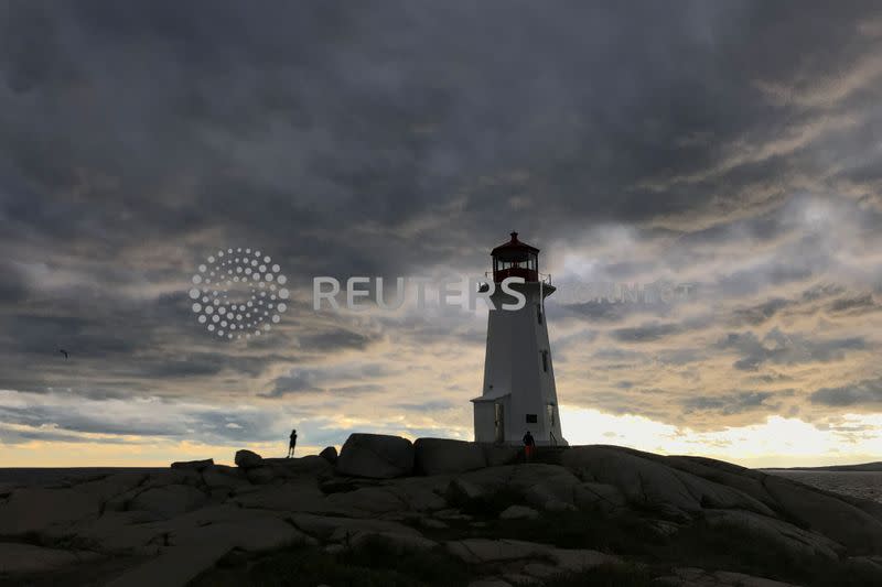 People walk on the rocks at the lighthouse at dusk in Peggy's Cov