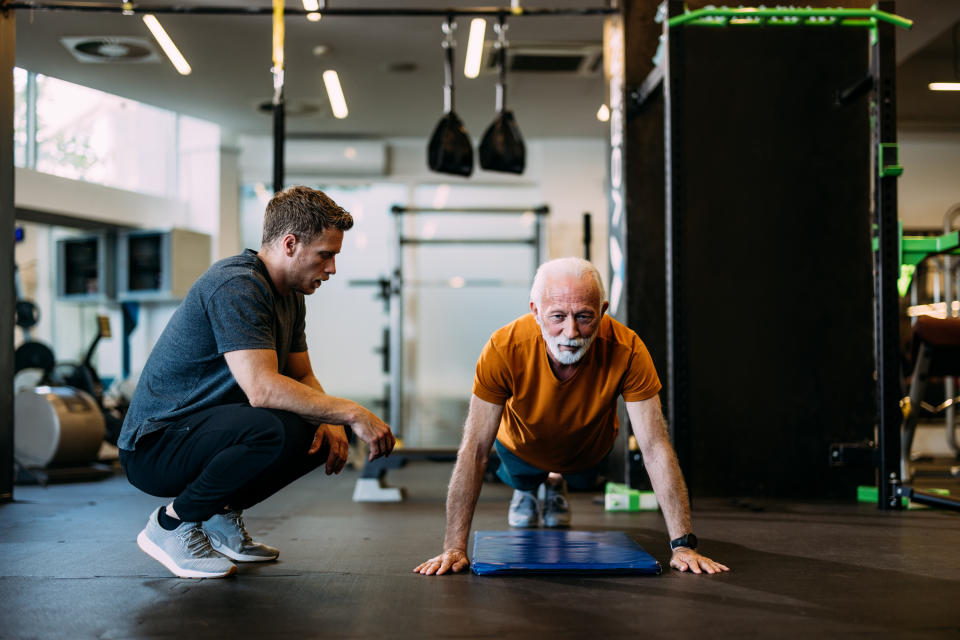 Senior man performing push-ups with the guidance of a personal trainer in a modern gym setting.